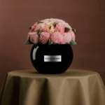 Black ceramic vase named "Minga Honey" with fluffy pink peonies bouquet on beige cloth-covered table