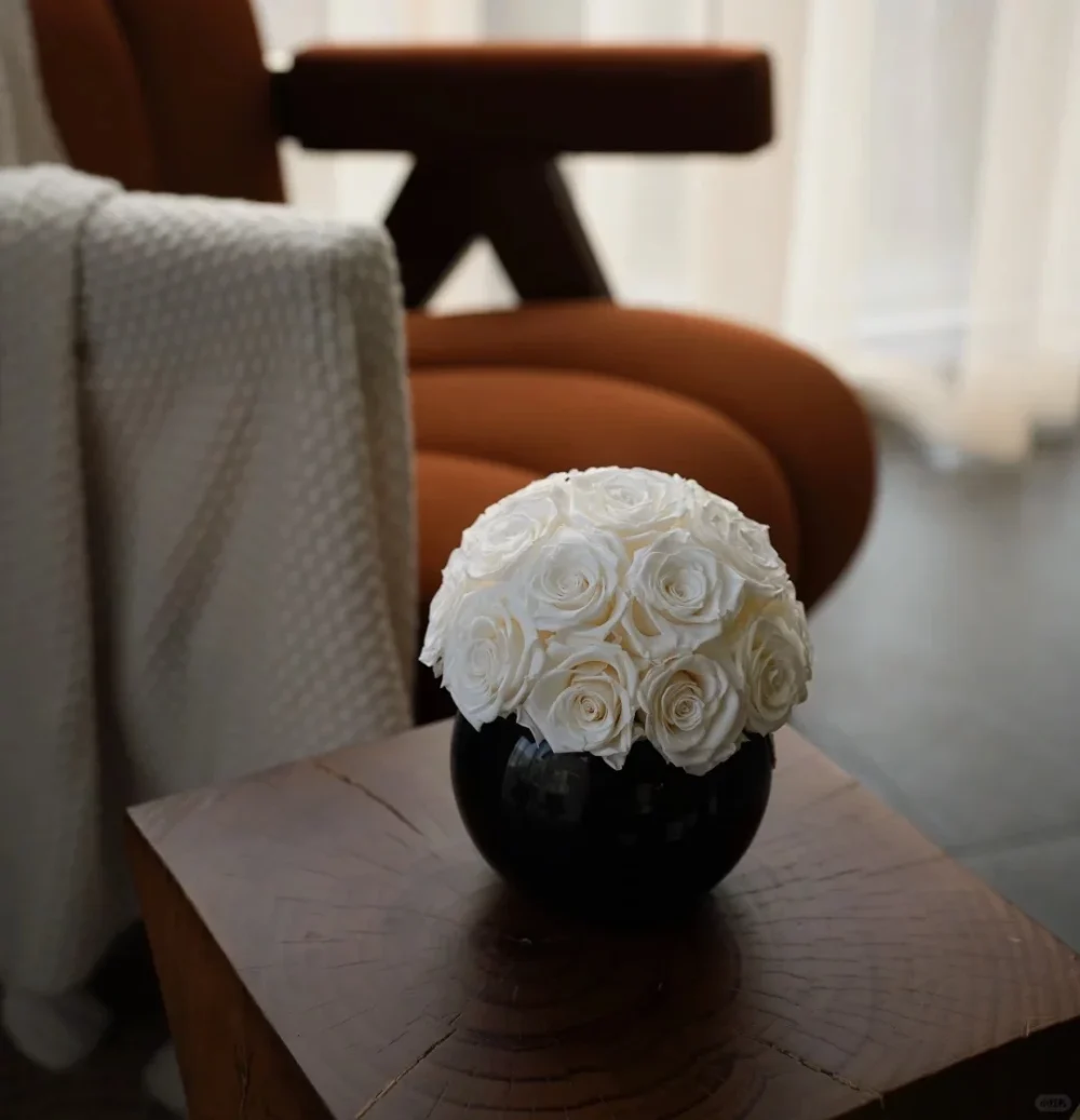 Black ceramic vase with white faux roses on wooden side table