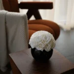 Black ceramic vase with white faux roses on wooden side table