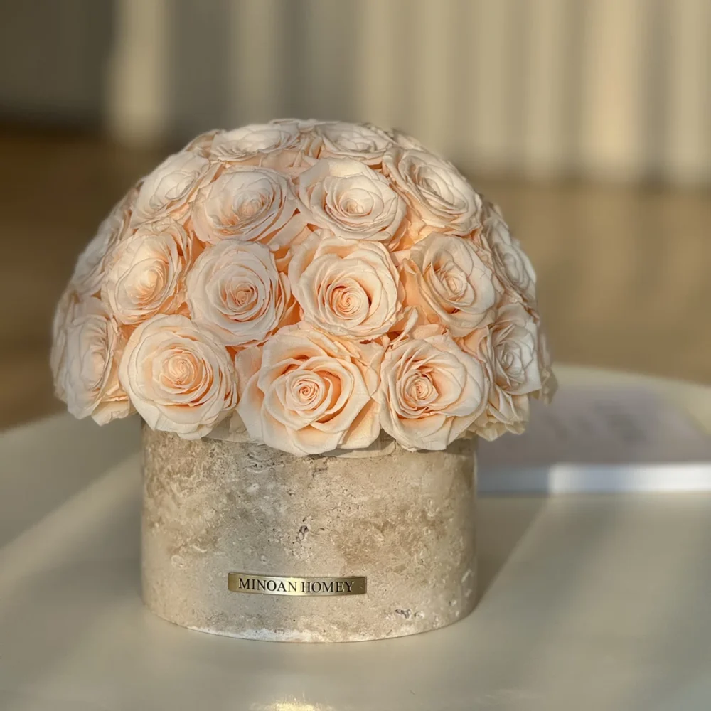 Round beige ceramic vase labeled "MIRAX HOMME" with pale peach rose bouquet on white surface