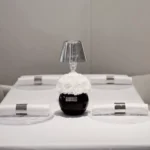 Minimalist dining table setting with small black vase containing white floral arrangement and silver-rimmed plates