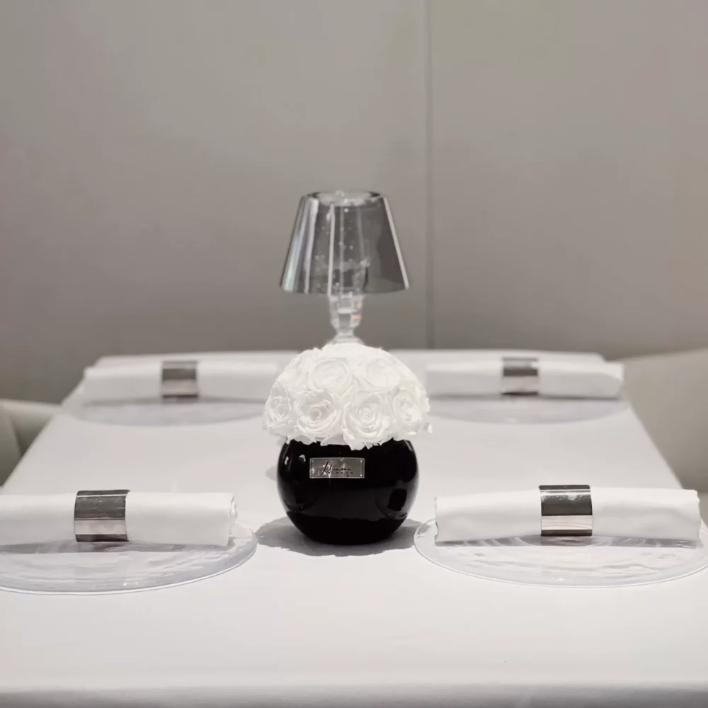 Minimalist dining table setting with small black vase containing white floral arrangement and silver-rimmed plates