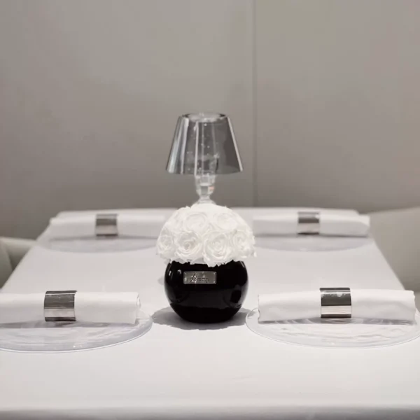 Minimalist dining table setting with small black vase containing white floral arrangement and silver-rimmed plates