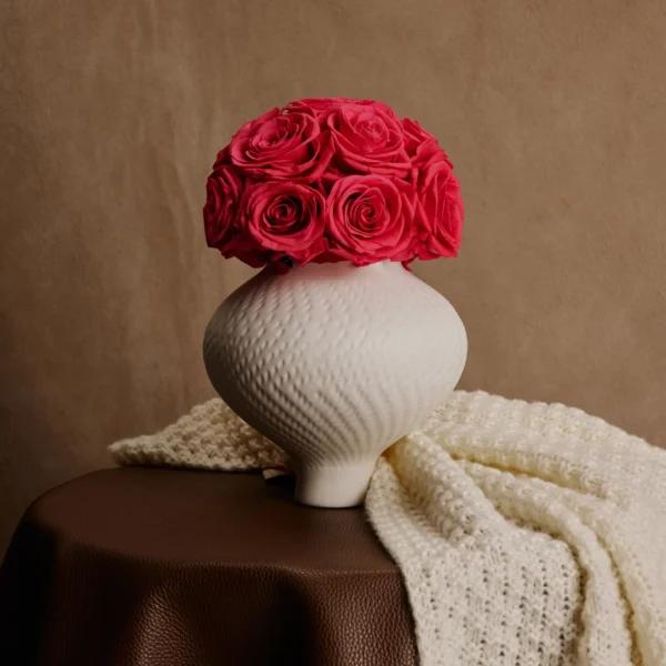 White ceramic textured vase with vibrant red roses on brown leather tablecloth creating rustic atmosphere
