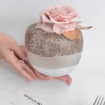 Small spherical jar with chia pudding and pink artificial rose on white surface