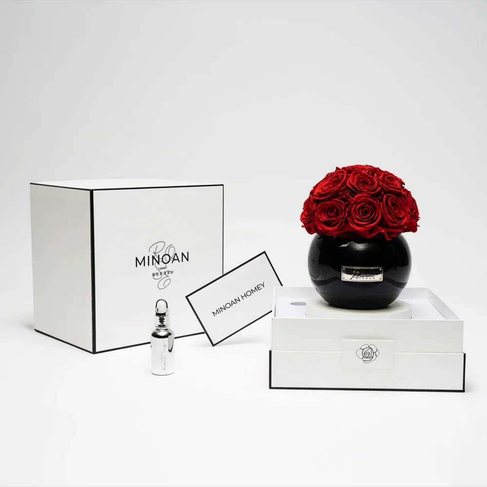 Luxurious minimalist setting with black vase of red roses and "Minoan" branded products on white studio setup
