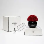 Luxurious minimalist setting with black vase of red roses and "Minoan" branded products on white studio setup